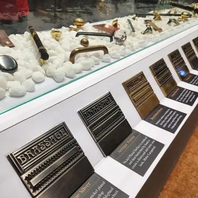 A close-up of our finish sample tiles on display at an exhibition. Each tile is a substantial piece of solid brass, showcasing the true color and texture of finishes like Antique Silver, Antique Pewter, and Burnished Brass.