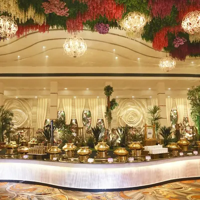 An opulent wedding reception setup featuring a grand, curved buffet line with traditional brass serveware, set under a stunning floral ceiling. This demonstrates our capability for large-scale, luxurious events.