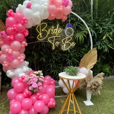 A beautiful outdoor 'Bride to Be' setup with a custom neon sign, surrounded by a lush pink and white balloon garland. This is perfect for a bridal shower or bachelorette party.