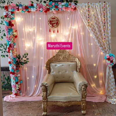 A full view of my Tapasvi homecoming setup, featuring a throne, a lit backdrop with a floral arch, and a printed curtain. This creates a perfect spot for photos and for the family to honor the Tapasvi.
