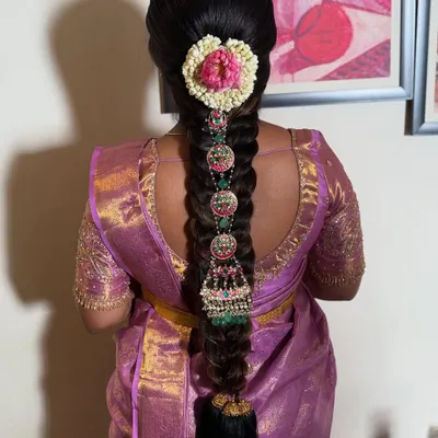 A stunning South Indian bridal braid featuring intricate temple jewelry and a floral heart design made with jasmine and rose petals. This is a perfect example of a traditional yet personalized bridal look.