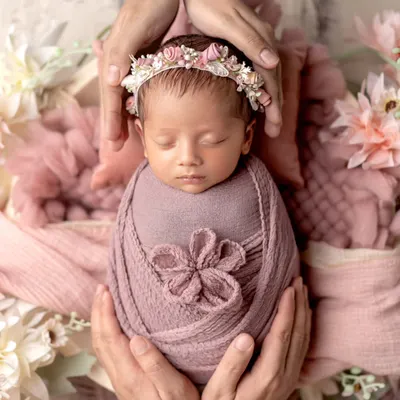 A perfect little angel, wrapped in pink and crowned with flowers. This classic newborn pose, with the baby cradled in parents' hands, is a timeless way to remember how small they once were.