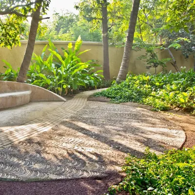 From a past project, this image shows a custom-paved walkway made with local stone. The swirling pattern mimics natural forms and is integrated with a built-in seating area, surrounded by tropical plants.