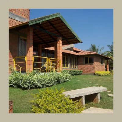 This farmhouse design uses hollow clay blocks and a sloping Mangalore tile roof to create a modern home with a strong vernacular feel. The open verandah and stone bench invite outdoor living, blurring the lines between the house and the lawn.