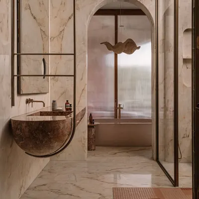 This junior master ensuite at Rehethaan is a moody, atmospheric space. A sculptural red marble sink appears to float, framed by an arched niche that leads to a private bathtub area.