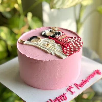 A side view of the first anniversary cake, showing the hand-piped illustration of the couple in their wedding attire on a smooth pink buttercream canvas.