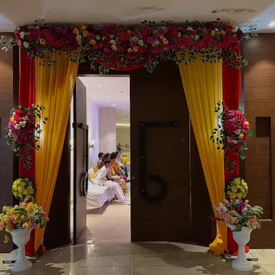 An impressive entrance I created for a banquet hall, using red and yellow drapes with large floral bouquets. It frames the doorway beautifully and sets a grand tone for the event inside.