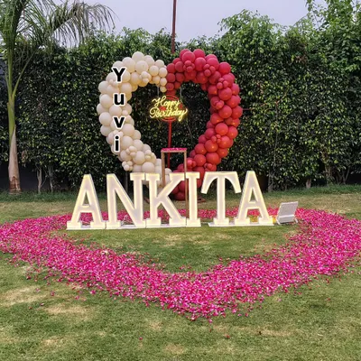 Make a statement with a grand outdoor decoration. This setup in a garden features large, light-up marquee letters spelling a name, a heart-shaped balloon arch, and a huge heart made of rose petals on the grass.