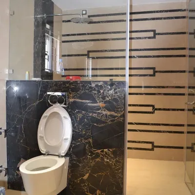 A luxurious bathroom design featuring a bold combination of black marble and patterned beige wall tiles. A seamless glass partition separates the wet and dry areas, and a wall-mounted toilet enhances the modern, clean aesthetic.