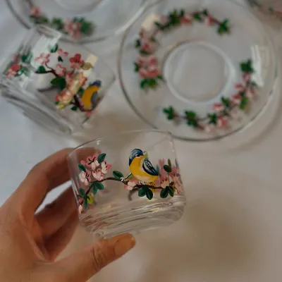 A close-up of our hand-painted glass teacup featuring a delicate yellow bird perched on a cherry blossom branch. Each detail is painted with fine brushes to bring the scene to life.