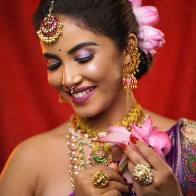 A beautiful bridal portrait where the hair is styled in a neat updo adorned with fresh lotus petals. This hairstyle allows the focus to be on the bride's expression and her intricate jewelry.