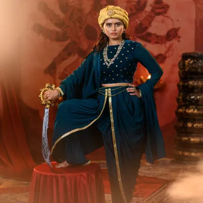 A powerful, full-length portrait of our Rani Lakshmibai recreation. The commanding stance on the pedestal, with sword in hand, captures the warrior queen's indomitable spirit against a dramatic backdrop.