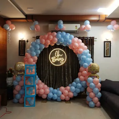 A wider view of the at-home baby shower setup, showing how the large circular balloon arch fits perfectly within a living room. The design includes 'BABY' blocks and balloon pillars with baby-themed foils.