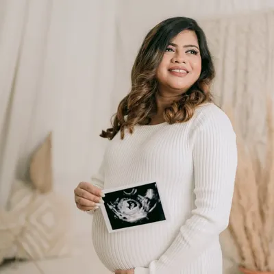 A portrait of a glowing mother-to-be. Holding her sonogram picture, she looks towards the future with a happy and hopeful expression, beautifully captured in a bright, airy studio.