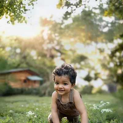 A toddler exploring a sunlit garden, crawling on the grass with a joyful smile. This is the magic of letting children be little, capturing their pure curiosity in the warm glow of natural light.