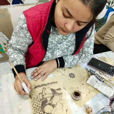 A student practicing the fine lines of Kalamkari painting, a traditional art form that involves freehand drawing and natural dyes.