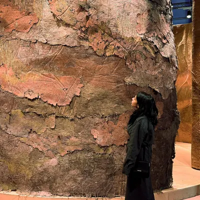 A visitor contemplates the monumental textures of our 'Soil' installation. We abstracted the story of soil into varied layers of embracing surfaces, with debossed roots implying both its nurturing character and its quiet, primordial strength.