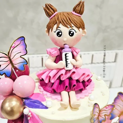 A close-up of a handmade fondant figurine for a first birthday cake. I teach how to sculpt expressive faces, create detailed clothing like this ruffled pink dress, and add small accessories like the milk bottle.