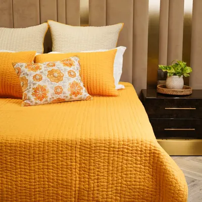 A beautifully made bed with vibrant yellow and orange bedding against a modern, textured headboard. This shot creates a warm and inviting atmosphere, perfect for showcasing a bold home collection.