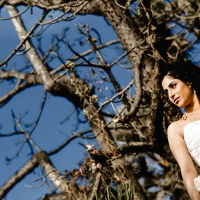 A quiet, contemplative portrait of a bride against a natural backdrop. The low angle and clear blue sky create a simple yet beautiful frame that highlights her elegance.