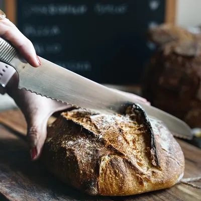 Slicing into this beauty is like unwrapping a gift. This action shot captures the satisfying moment of cutting into a freshly baked sourdough loaf, revealing the crusty exterior and soft crumb.