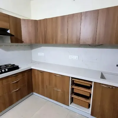 This L-shaped kitchen uses a beautiful wood laminate finish for all the cabinets, creating a warm and natural aesthetic. The design includes a pull-out wicker basket for vegetables and handle-free drawers.