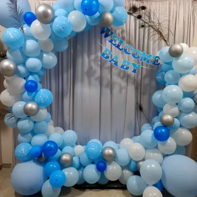 A beautiful circular balloon arch in shades of blue, white, and silver, with a 'Welcome Baby' banner. This setup is perfect for creating a photo corner at home.