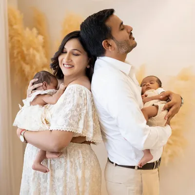 Welcoming newborn twins is double the blessing. In this serene studio portrait, a new mother and father stand back to back, each cradling one of their tiny miracles, capturing a moment of quiet joy and connection.