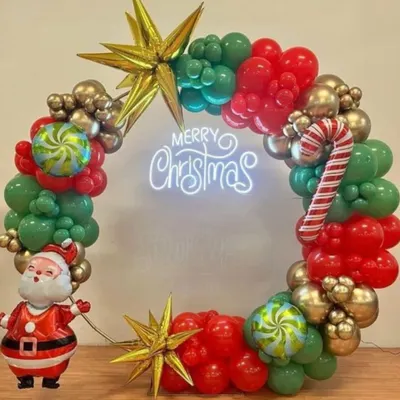 A festive Christmas wreath made entirely of balloons. This one features red, green, and gold balloons, a 'Merry Christmas' neon sign, star-shaped foils, and a cute Santa Claus figure.