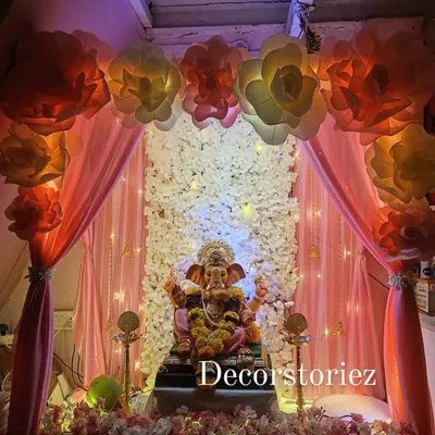A complete and immersive Ganpati decoration featuring a stunning backdrop of white flowers and peach drapes. The setup is beautifully lit to highlight the idol and create a warm, festive glow in the home.