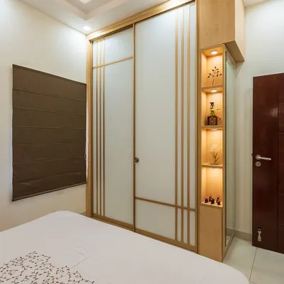 A serene bedroom featuring a sliding wardrobe with frosted glass and wood inlay. The design includes an integrated open shelving unit with warm lighting, perfect for displaying small treasures.