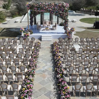 An aerial view showcasing the perfect symmetry of this pastel floral wedding ceremony. The aisle, lined with lush ground-level arrangements, leads the eye directly to the magnificent mandap, creating a breathtaking journey for the bride's entrance.