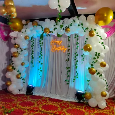 This jungle or nature-themed birthday backdrop is perfect for a first birthday. We use a white balloon arch decorated with green vines, a 'Happy Birthday' neon sign, and blue uplighting to create an enchanting forest look.