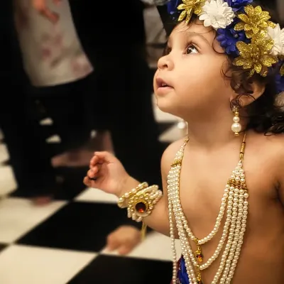 A candid shot of a young child in a Krishna costume, looking up with wonder. This is the essence of genuine childhood photography, capturing their natural curiosity during a festival celebration.