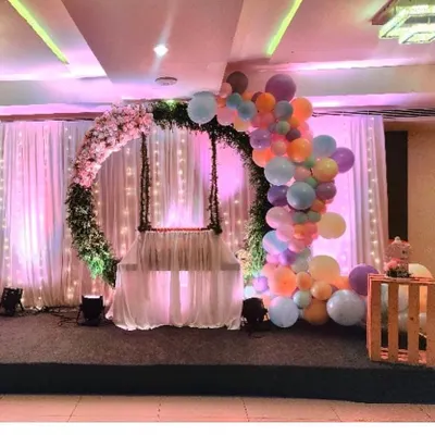 An ethereal cradle ceremony setup featuring a floral wreath and a cascade of pastel balloons. The soft lighting and elegant swing create a perfect, serene atmosphere for this special occasion.