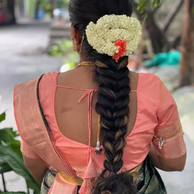 A classic South Indian bridal braid, neatly woven and adorned with a semi-circle of fresh jasmine and a touch of orange kanakambaram flowers. This hairstyle is timeless and elegant.