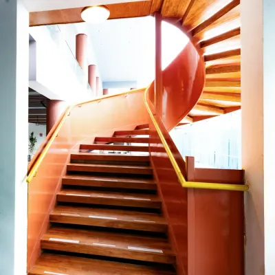 The striking spiral staircase at the Sona Vistaas Clubhouse, seen from a lower angle. Its continuous, flowing form in a bold terracotta red acts as a sculptural centerpiece, seamlessly blending movement, structure, and visual drama within the multi-level space.