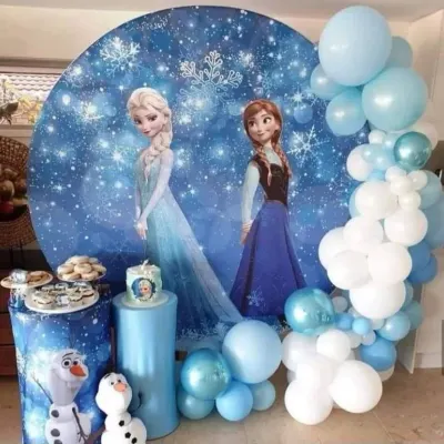 A magical Frozen themed birthday party featuring Elsa and Anna on a sparkling winter backdrop. The decor is completed with a blue and white balloon garland and themed pedestals for the cake and treats.