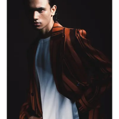A tight, intimate portrait from the 'Silhouette' series, where dramatic light falls across half of the model's face. The deep shadows create a powerful, moody atmosphere that emphasizes his features and the texture of the jacket.