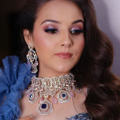 A close-up of a stunning cocktail look. The focus is on the shimmery blue and purple smokey eye, which beautifully complements the client's blue outfit and diamond jewelry.