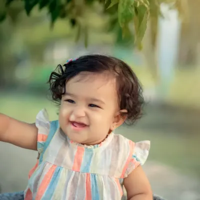 A beautiful outdoor portrait capturing a moment of pure, uninhibited laughter. The natural light and green background make this little girl's happy expression shine even brighter.