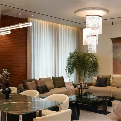 A complete view of the living and dining area at our Amaryllis project, showcasing the layered lighting from the sculptural chandelier and linear pendant. The space is unified by earthy tones and an exposed brick wall, creating a warm, cohesive environment.