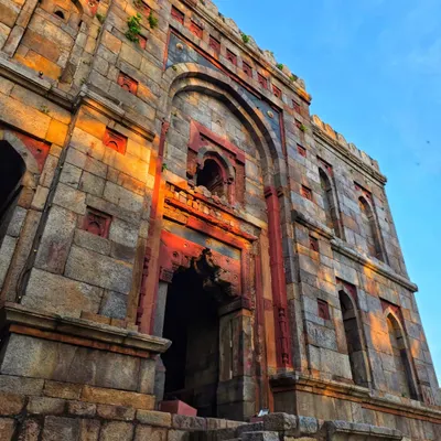 An upward shot of the stunning architecture at Lodi Garden, with the golden hour sun casting a warm glow on the ancient stone. This shows the beauty of Delhi's monuments.