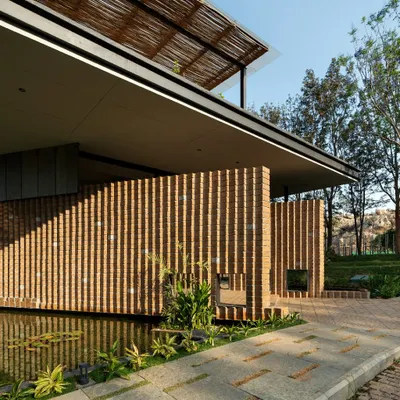 The entrance to 'The Earth' showcases its signature pleated walls made from Compressed Stabilised Earth Blocks (CSEB). The texture and warmth of the brick are balanced by a calm water feature and stone pavers, immediately grounding the building in its natural setting.