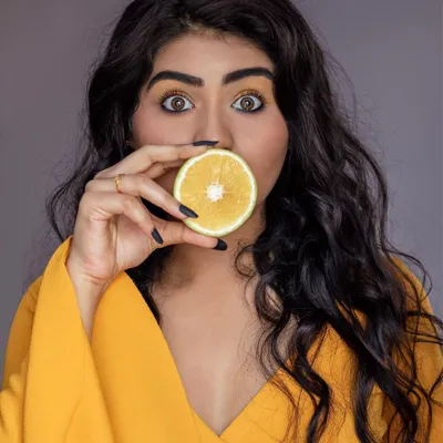 A fun and quirky close-up portrait using a slice of orange. The bright yellow of the fruit, outfit, and eyeshadow creates a vibrant, monochromatic theme that makes the model's expressive eyes the center of attention.