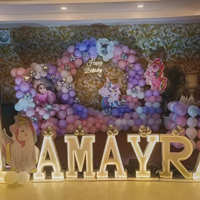A magical unicorn-themed first birthday for Amayra. The decor features a large balloon ring in pastel pink and purple, unicorn cutouts, and big, bright marquee letters for the name.