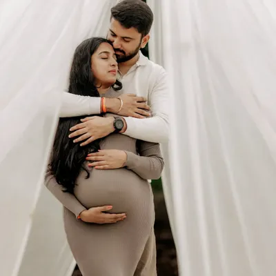 A quiet moment of connection as an expecting father gently holds his partner from behind. Set against soft white drapes, this image is all about the feeling of safety, love, and anticipation for their new arrival.