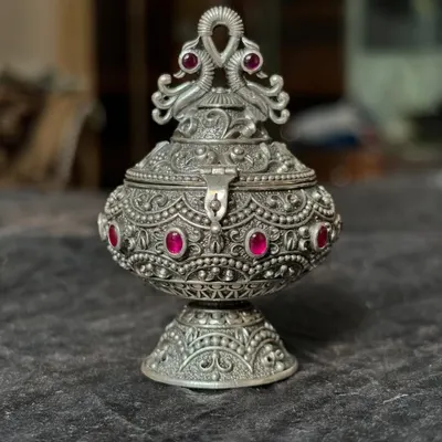 Our antique-finish silver kumkum box, shown closed to highlight the ornate peacock design on the lid. Studded with pink stones, this piece is a beautiful and traditional wedding or housewarming gift.