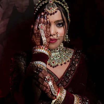 A striking portrait of a North Indian bride, using her henna-covered hand to create a sense of mystery and draw attention to her eyes. The dramatic lighting highlights her beautiful jewelry.