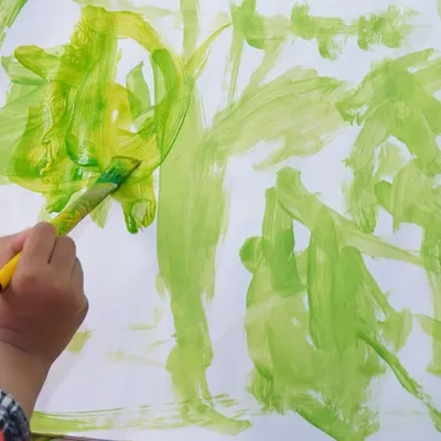 Little hands and busy minds at work. This close-up shows a child exploring shades of green, learning about color mixing and brush strokes in a free and expressive way.